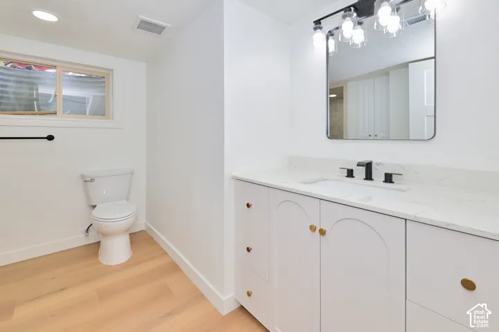 Vanity with stone countertop, undermount sink, matte black widespread faucet, arched cabinet detailing, and wood-finish flooring