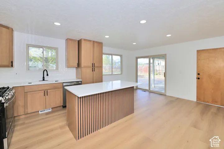 Kitchen featuring light wood-finish cabinetry, a central island with a slatted wood base and solid-surface countertop, wood-finish flooring, and recessed lighting