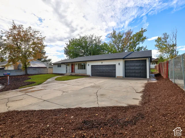 Ranch-style exterior featuring vertical white siding, two dark-toned garage doors, a concrete driveway, and established landscaping