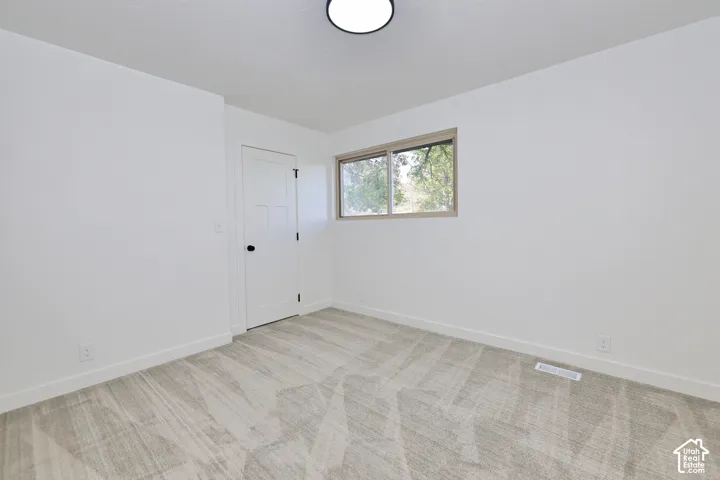 Neutral-toned wall-to-wall carpeting, clean white wall finishes, a single-panel interior door with matte black hardware, and a sliding window with neutral trim