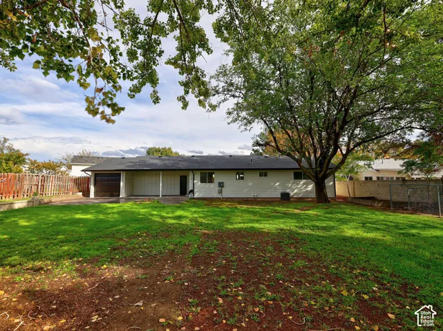 Single-story exterior featuring light-toned vertical siding, an attached garage, a covered porch, mature trees, and a spacious lawn