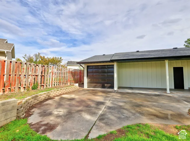 Detached single-car garage featuring vertical siding, shingle roofing, and a concrete driveway, complemented by a stone-block retaining wall and wood picket fencing