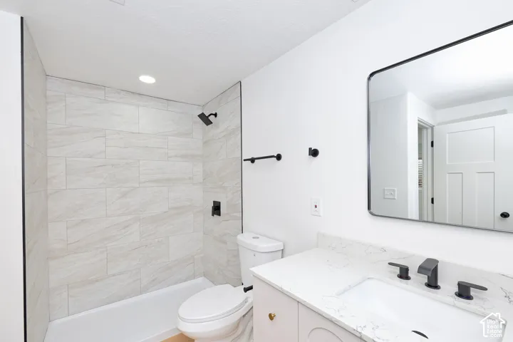 Bathroom featuring a shower surround with large-format stone-patterned tile, matte black fixtures, quartz countertop with an integrated basin, and a framed rectangular wall mirror