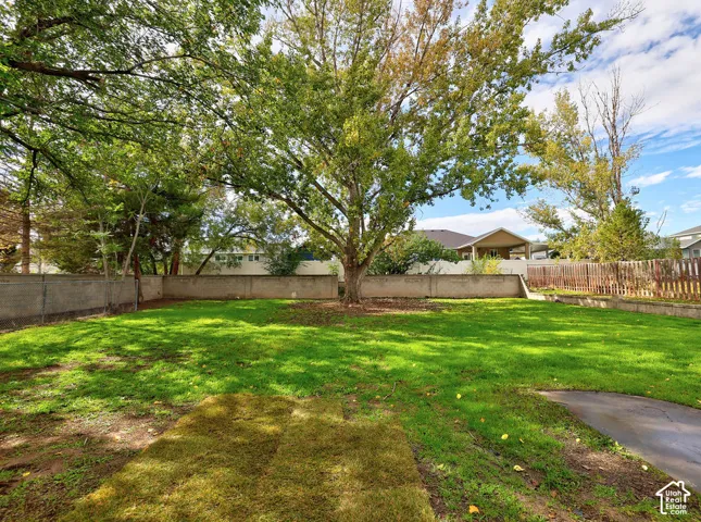 Backyard featuring a grass lawn, mature deciduous trees, and perimeter masonry wall fencing