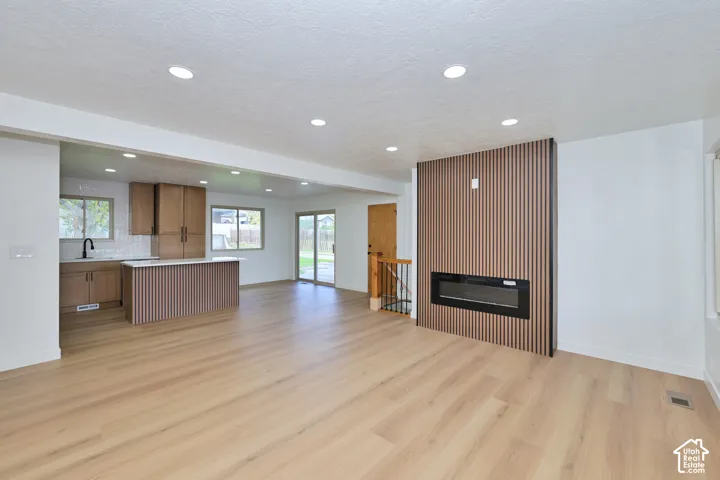 Wood-finish flooring, recessed lighting, linear electric fireplace with vertical slat wall detailing, and kitchen island with matching slat cabinetry