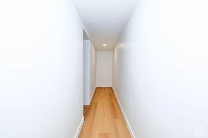 Hallway featuring wood-finish flooring, crisp white walls, and a recessed ceiling light