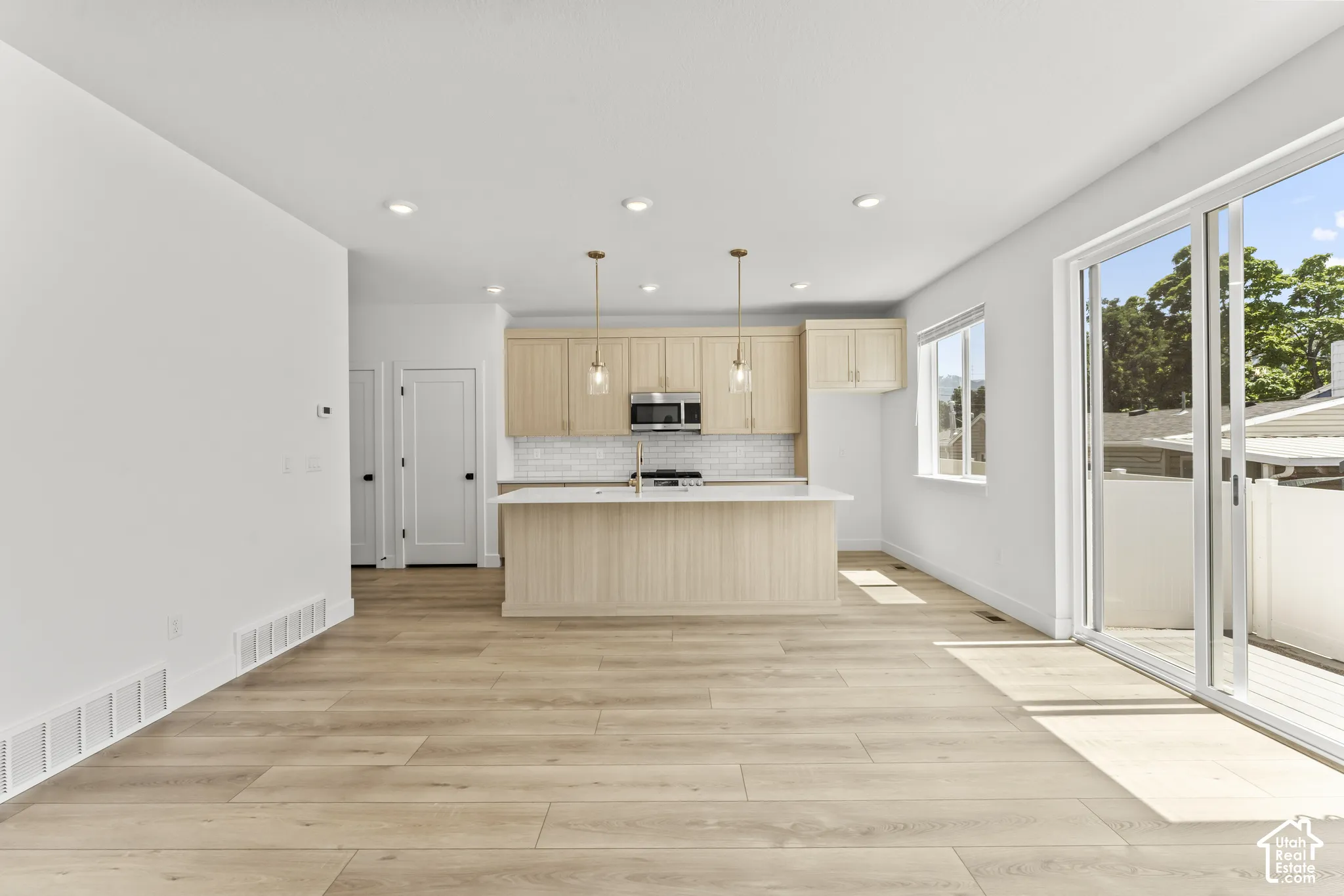 Kitchen featuring light-finish cabinetry, an island with countertop seating, a tiled backsplash, and recessed lighting, paired with wood-finish flooring and glass sliding doors