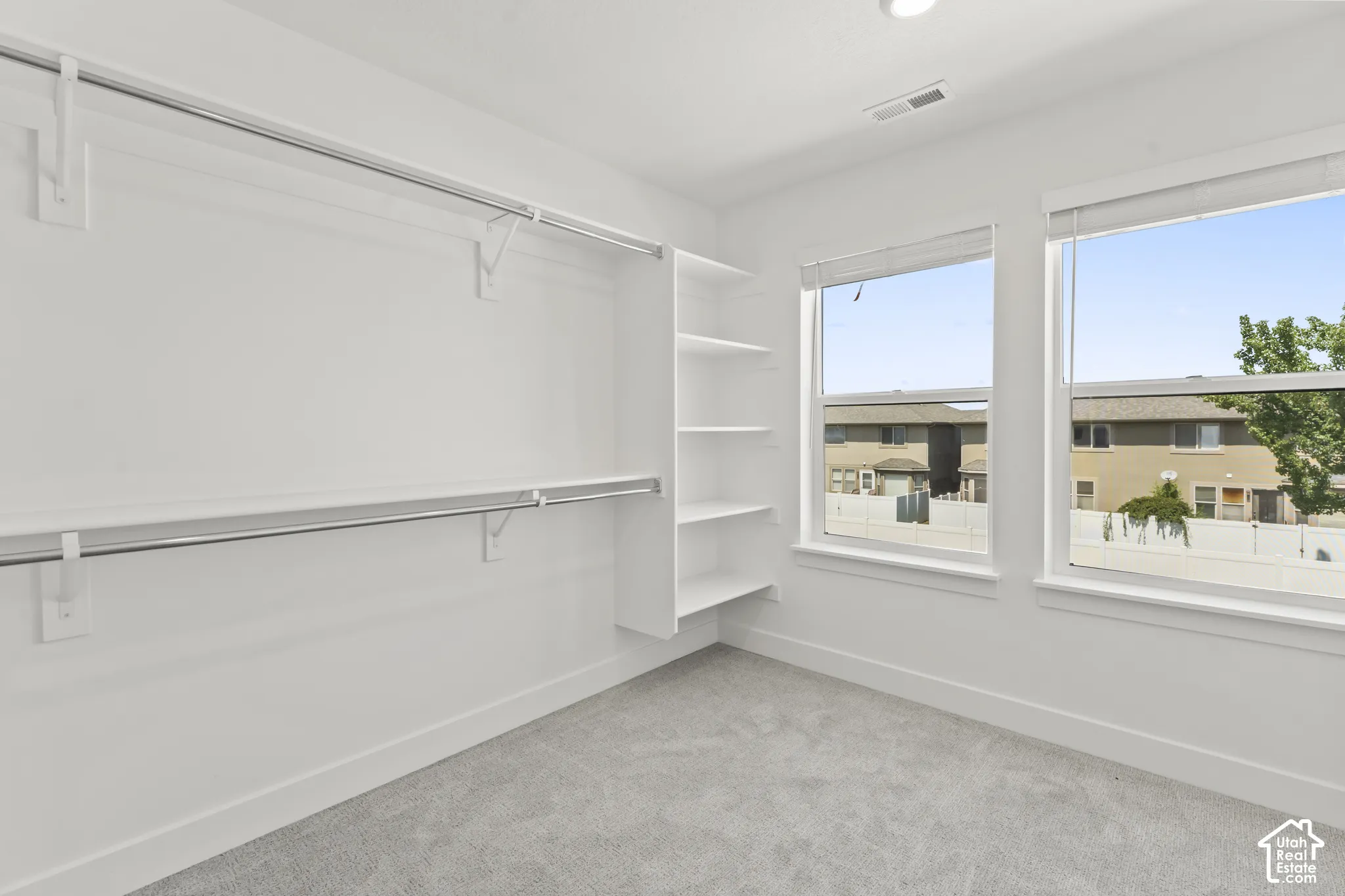 Walk-in closet featuring multi-level hanging rods, built-in shelving, gray carpeting, and dual windows