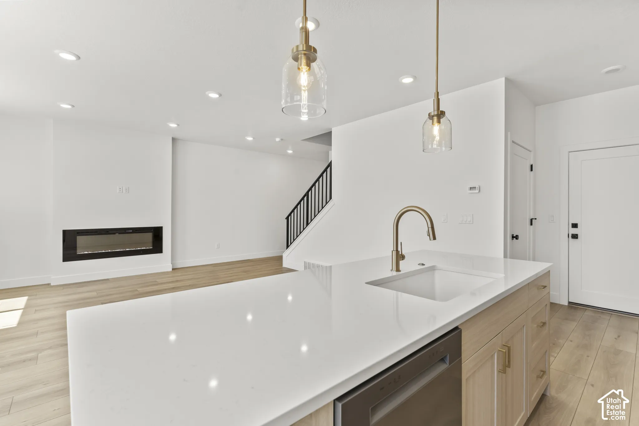 Kitchen island featuring light wood-finish cabinetry, white quartz countertop, and gold-tone faucet