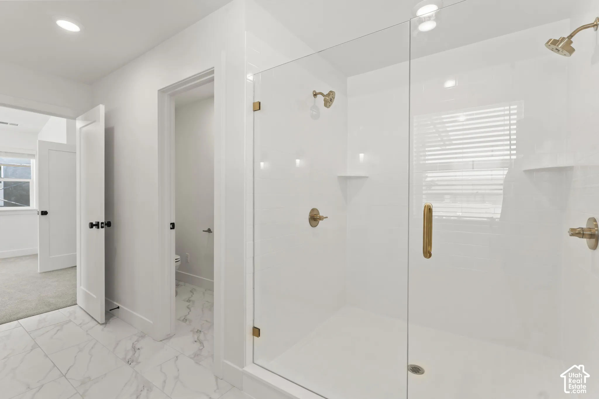 Walk-in shower featuring a glass enclosure, brass-finish fixtures, and built-in shelving, complemented by large-format tile flooring