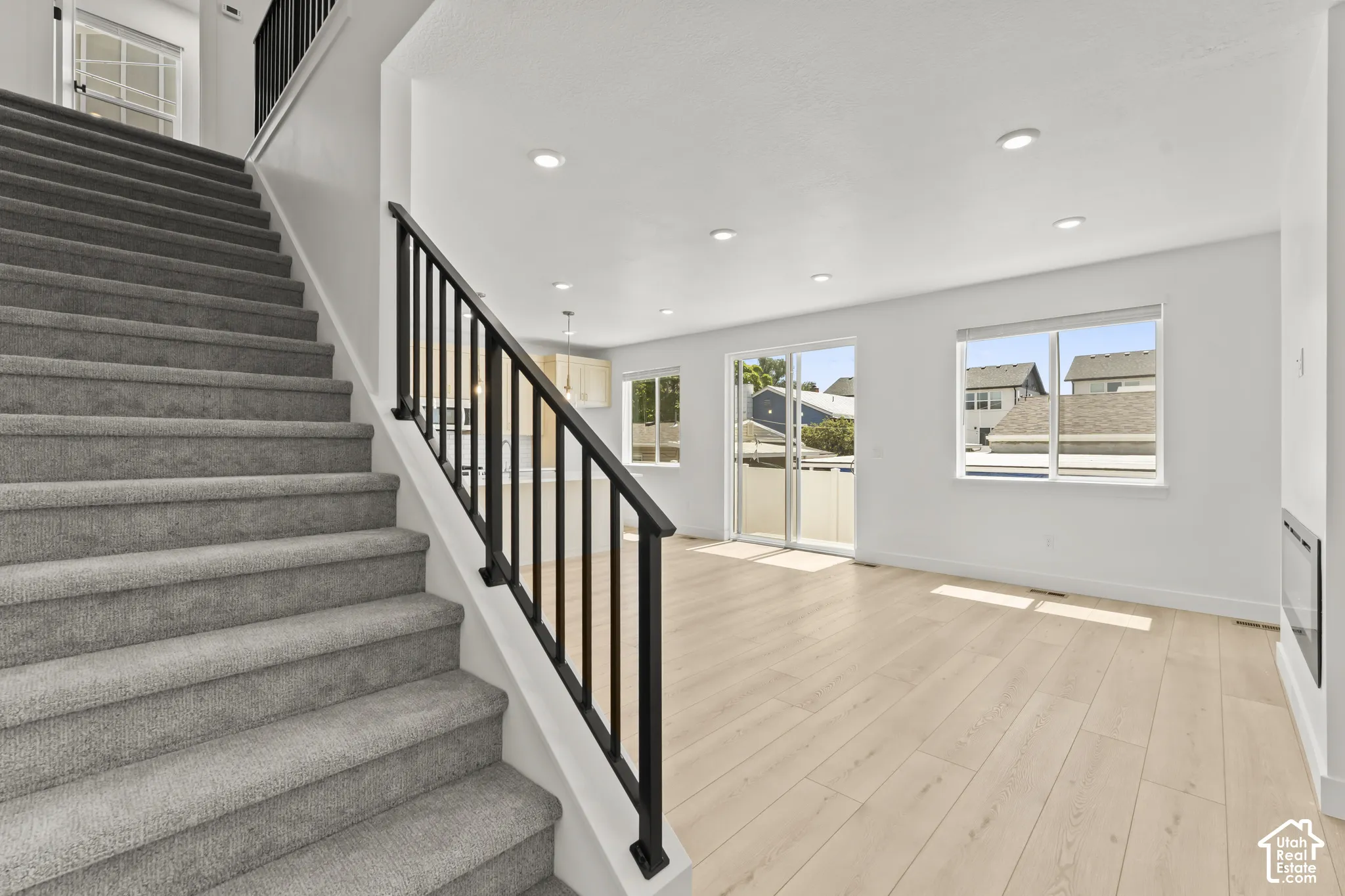 Staircase featuring carpeted steps and a matte black metal railing, light wood-finish flooring, recessed ceiling lighting, sliding glass door, and a wall-mounted fireplace