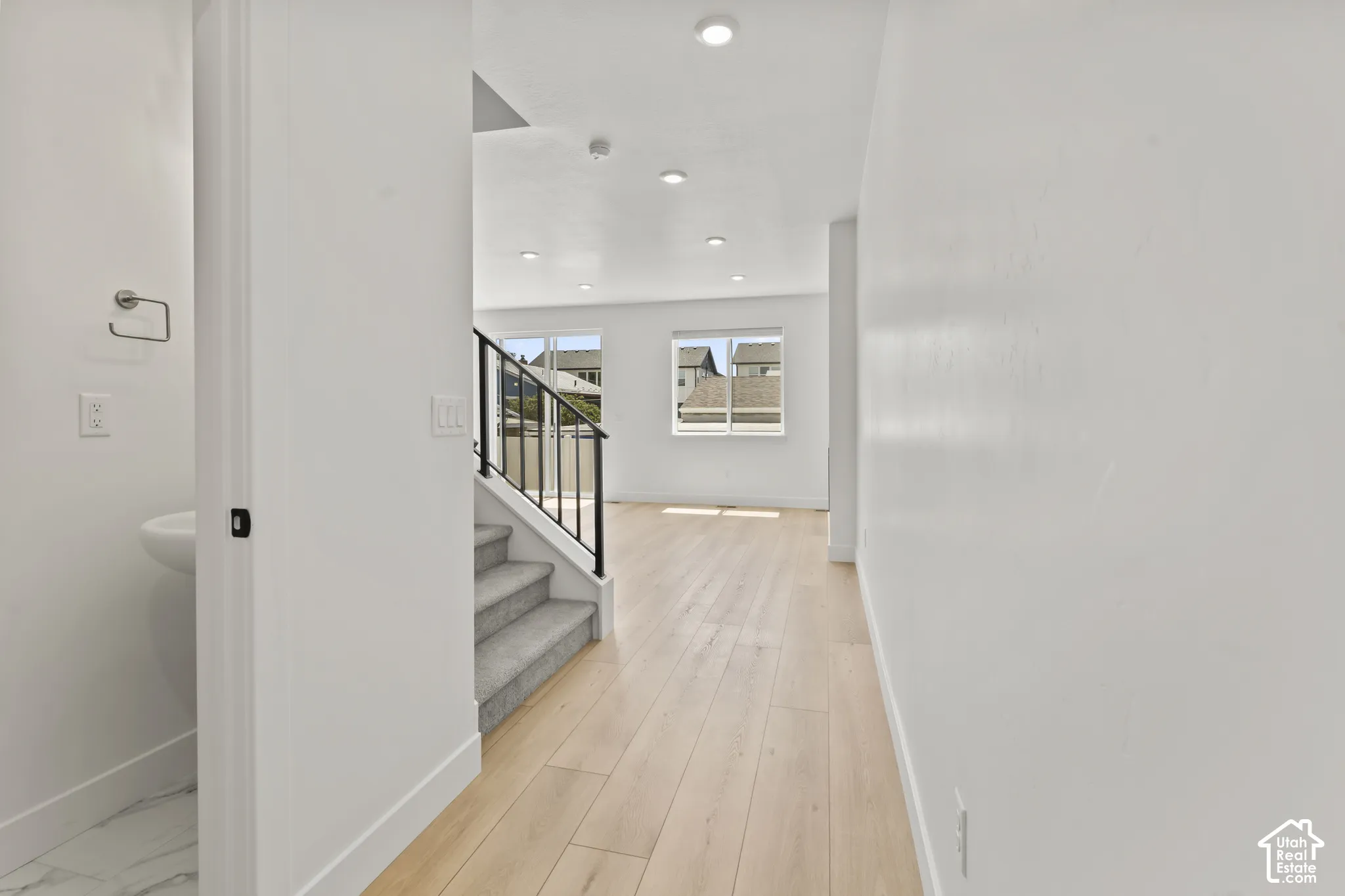 Interior space featuring wood-finish flooring, recessed lighting, carpeted staircase with a metal handrail, and a half-bathroom with a pedestal sink
