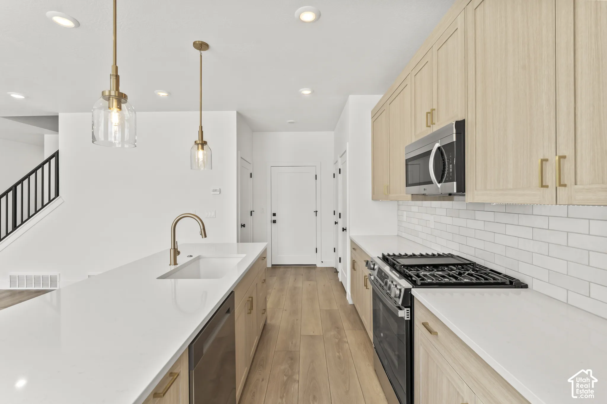 Kitchen featuring light wood-finish cabinetry, quartz countertops, white subway tile backsplash, stainless steel gas range, and wood-finish flooring