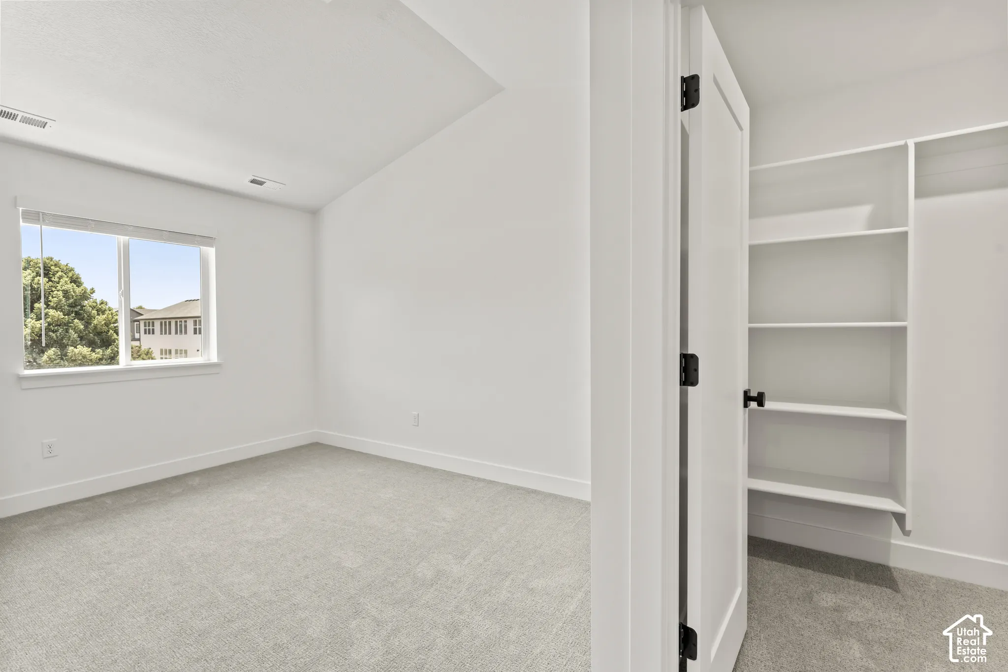 Vaulted ceiling, neutral wall-to-wall carpeting, single-pane window, and walk-in closet with built-in shelving