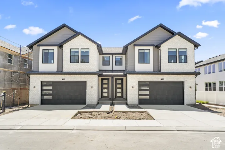 Two-story exterior featuring white brick veneer, grey horizontal siding, dual attached two-car garages with frosted glass panels, and modern entry doors with multi-pane windows