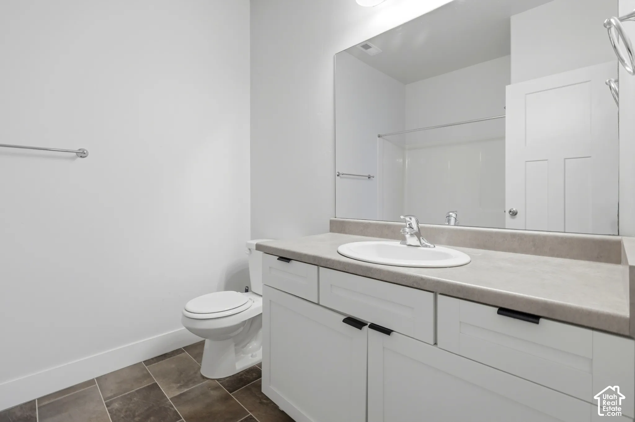 Bathroom featuring a white vanity cabinet with matte black hardware, stone-composite countertop with an integrated oval sink, full-width wall mirror, and tiled flooring