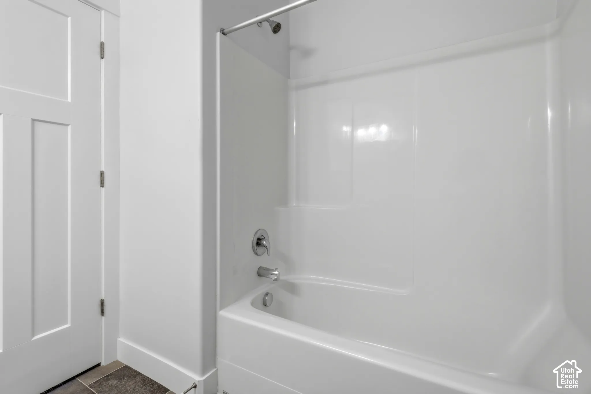 Built-in white tub and shower combination with a single-handle faucet, chrome showerhead, and solid-surface surround, featuring a three-panel interior door