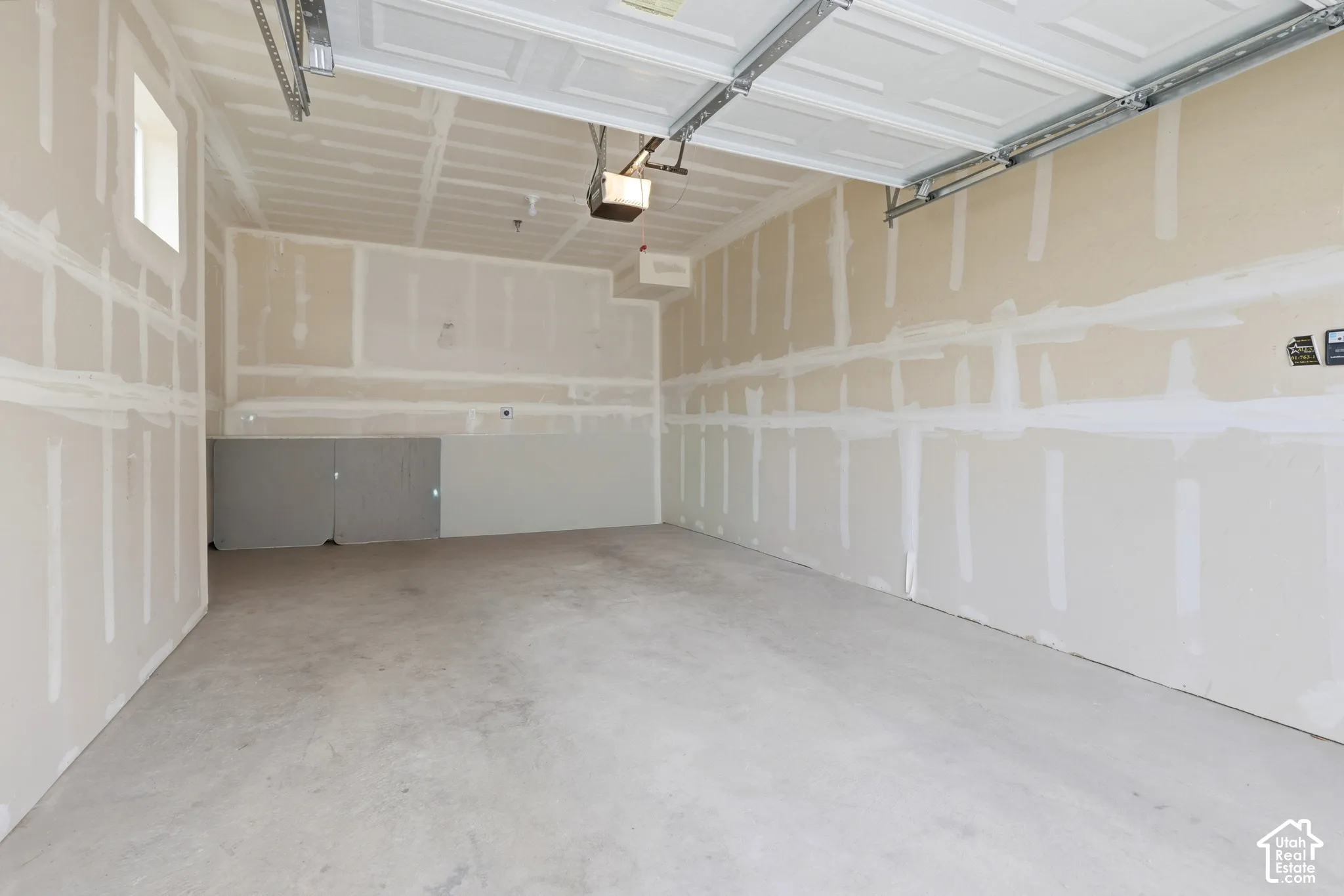 Attached garage featuring a concrete floor, high ceiling, wall-mounted garage door opener, and single-pane window