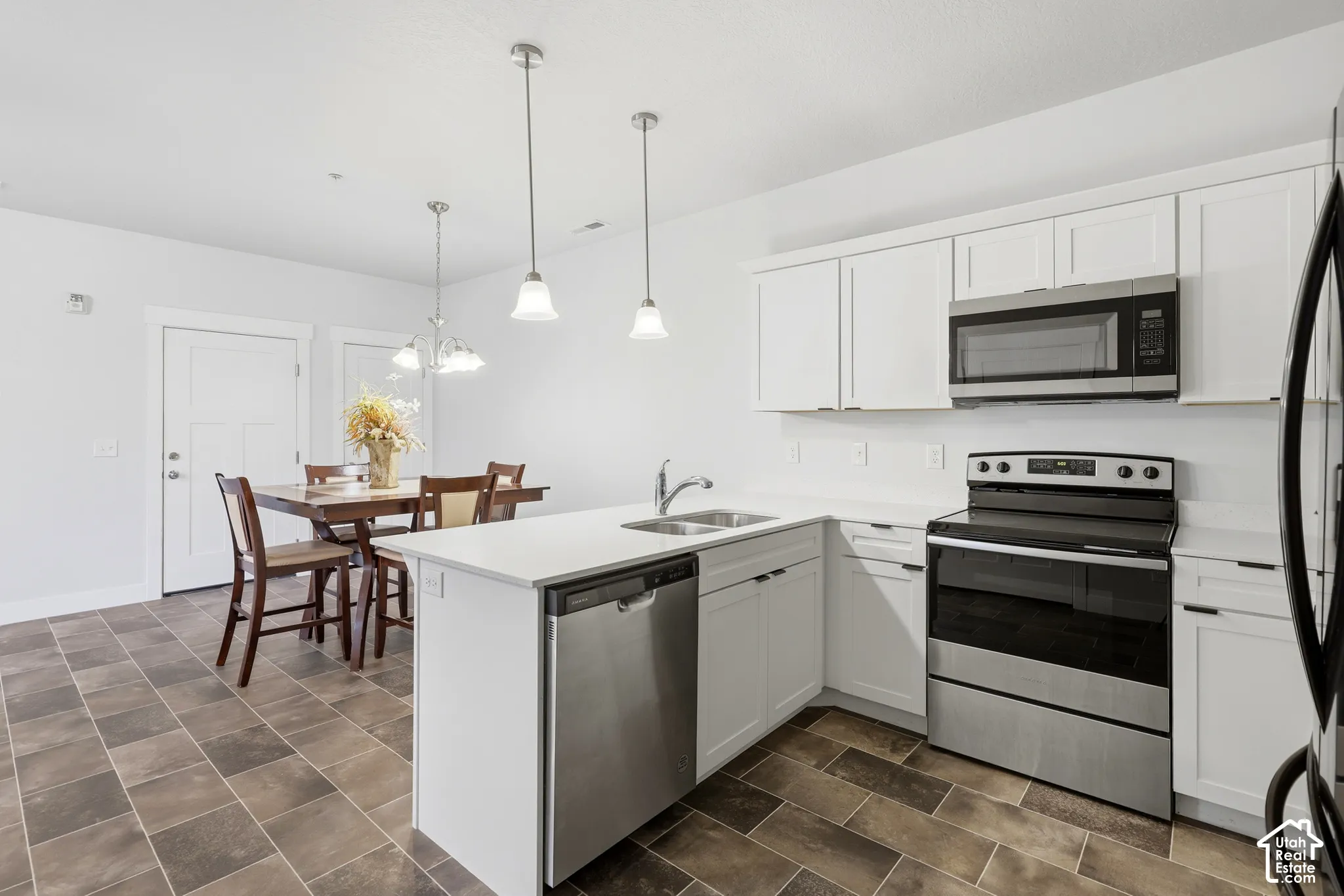 Kitchen featuring white cabinetry, stainless steel appliances, stone-finish countertops, dual-basin sink, and pendant lighting