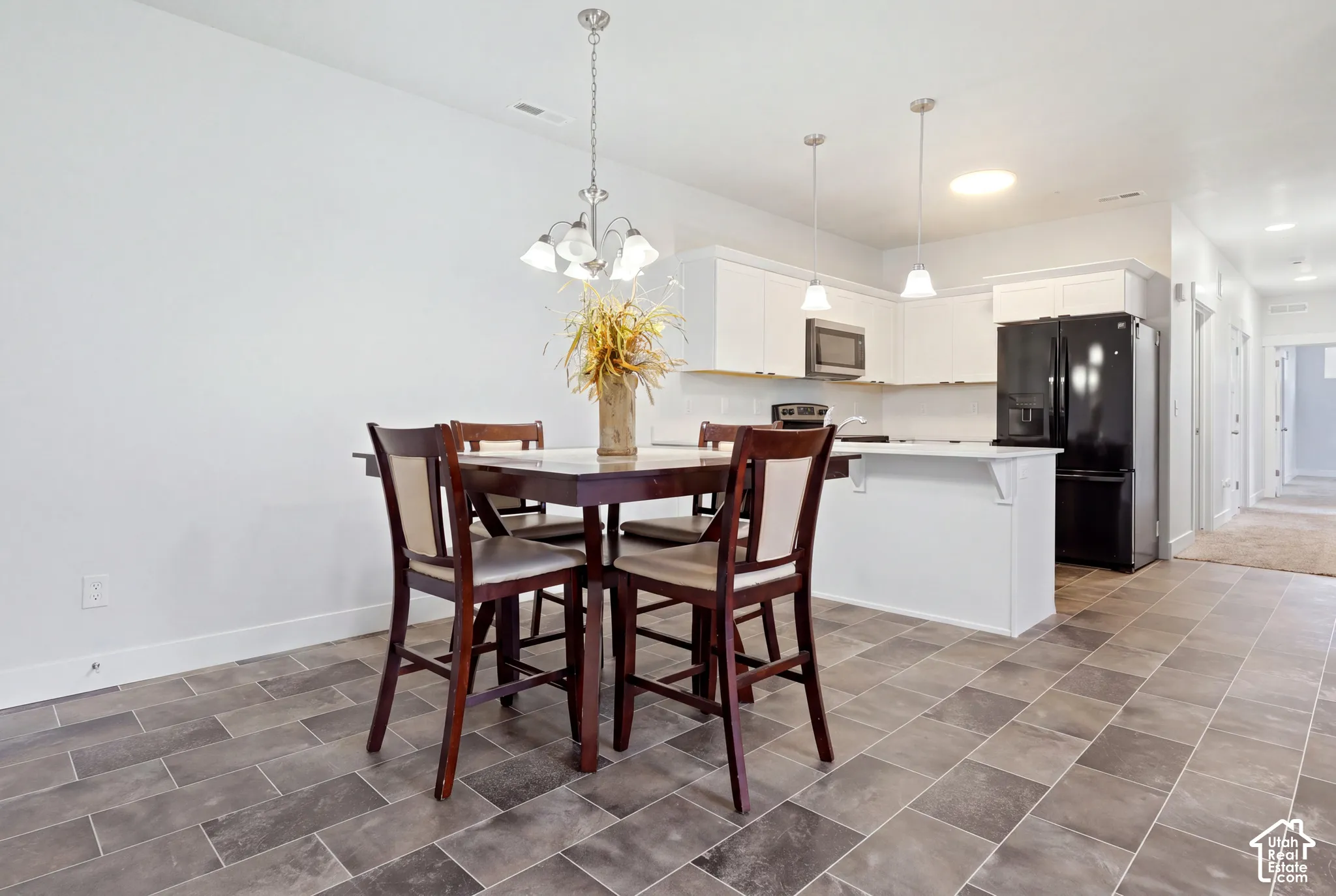 Kitchen featuring white shaker-style cabinetry, a breakfast bar, stone-finish tile flooring, and multi-light pendant fixtures