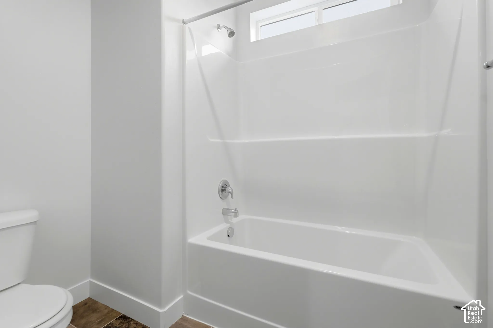 Bathroom featuring a white molded tub-and-shower surround with a chrome mixing valve and showerhead, a transom window, and wood-finish flooring