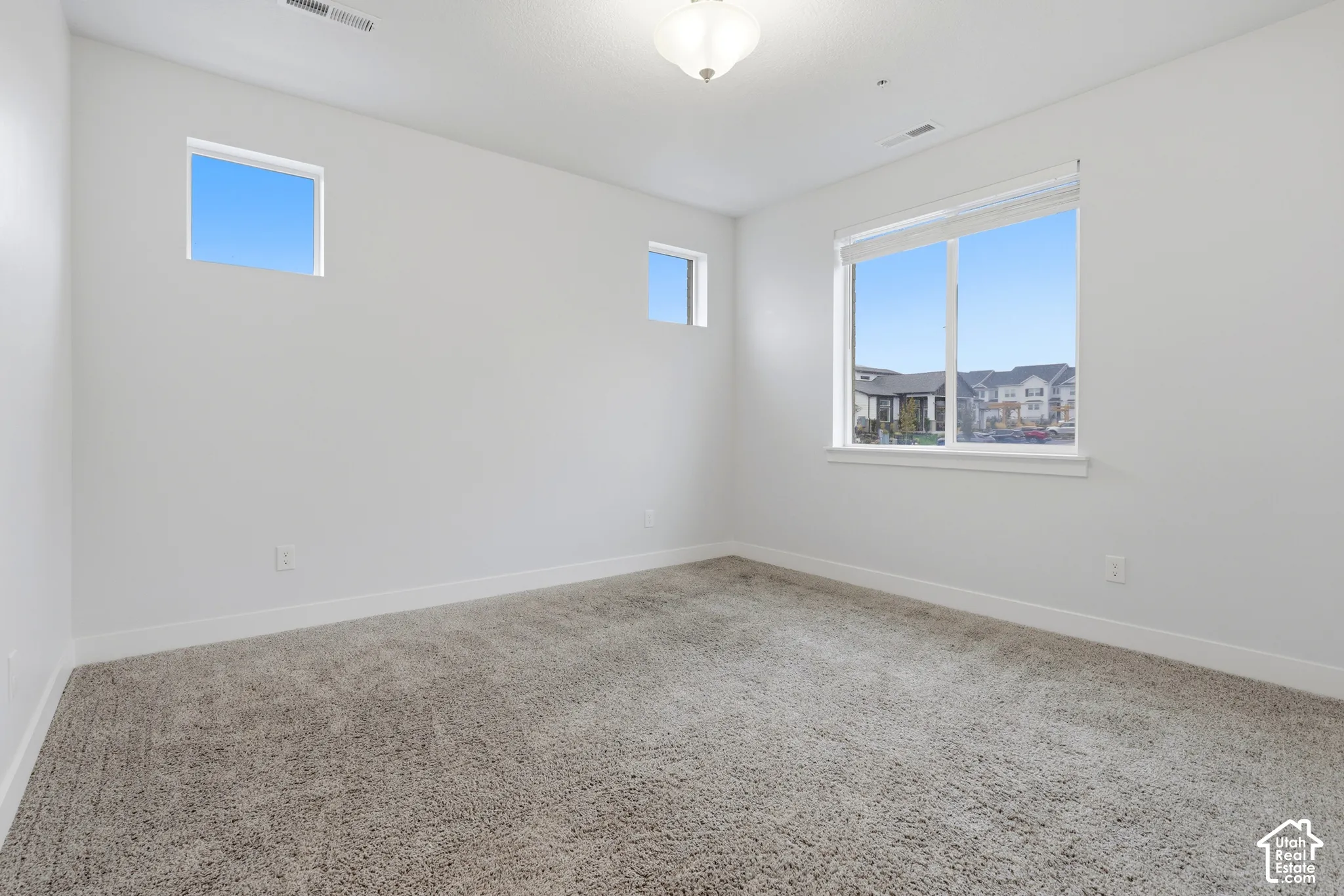 Neutral interior with wall-to-wall carpeting, two small square windows, one large rectangular window, and a ceiling-mounted light fixture