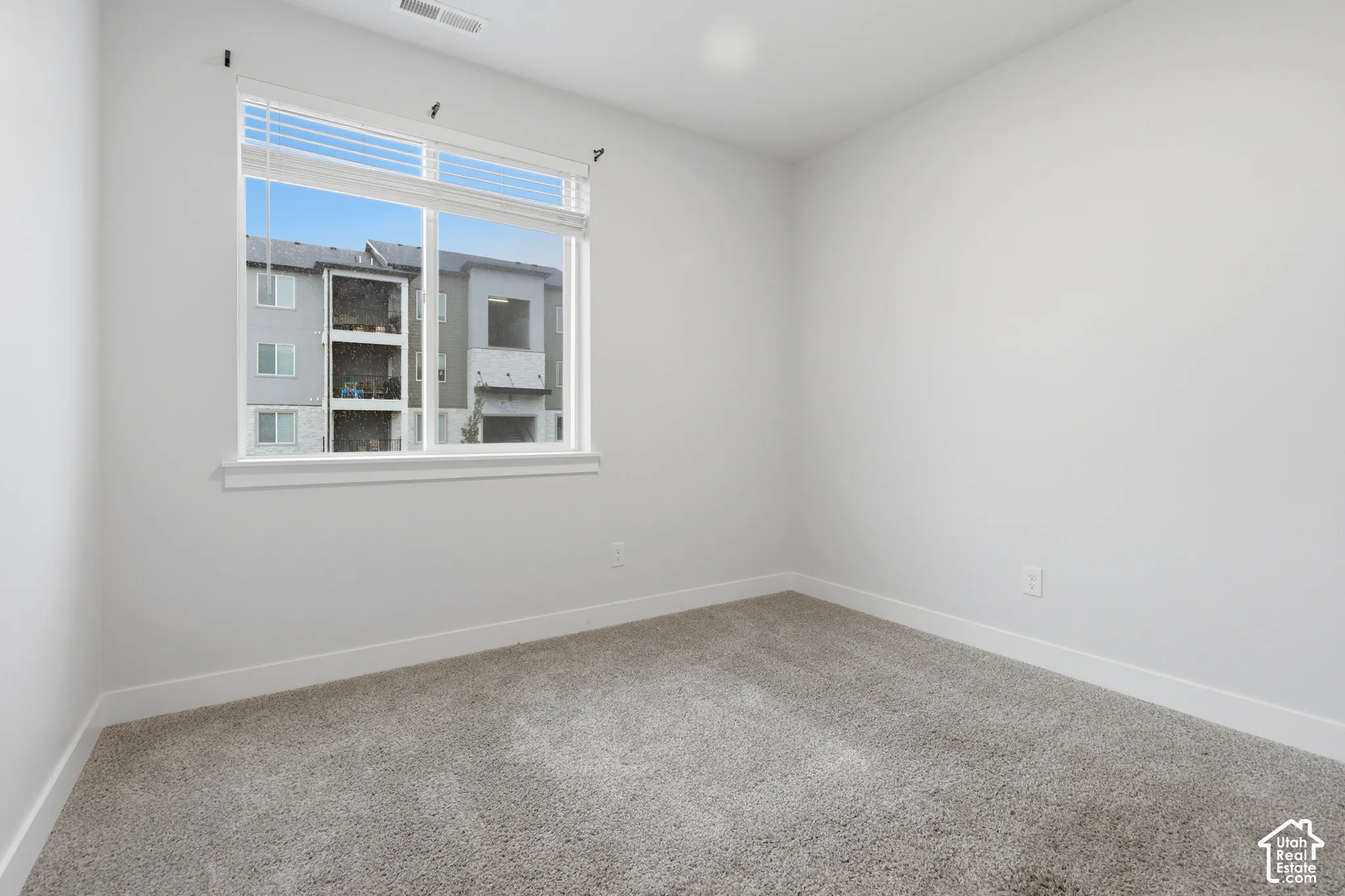 Neutral-toned interior space featuring plush carpeting and a large window with white blinds