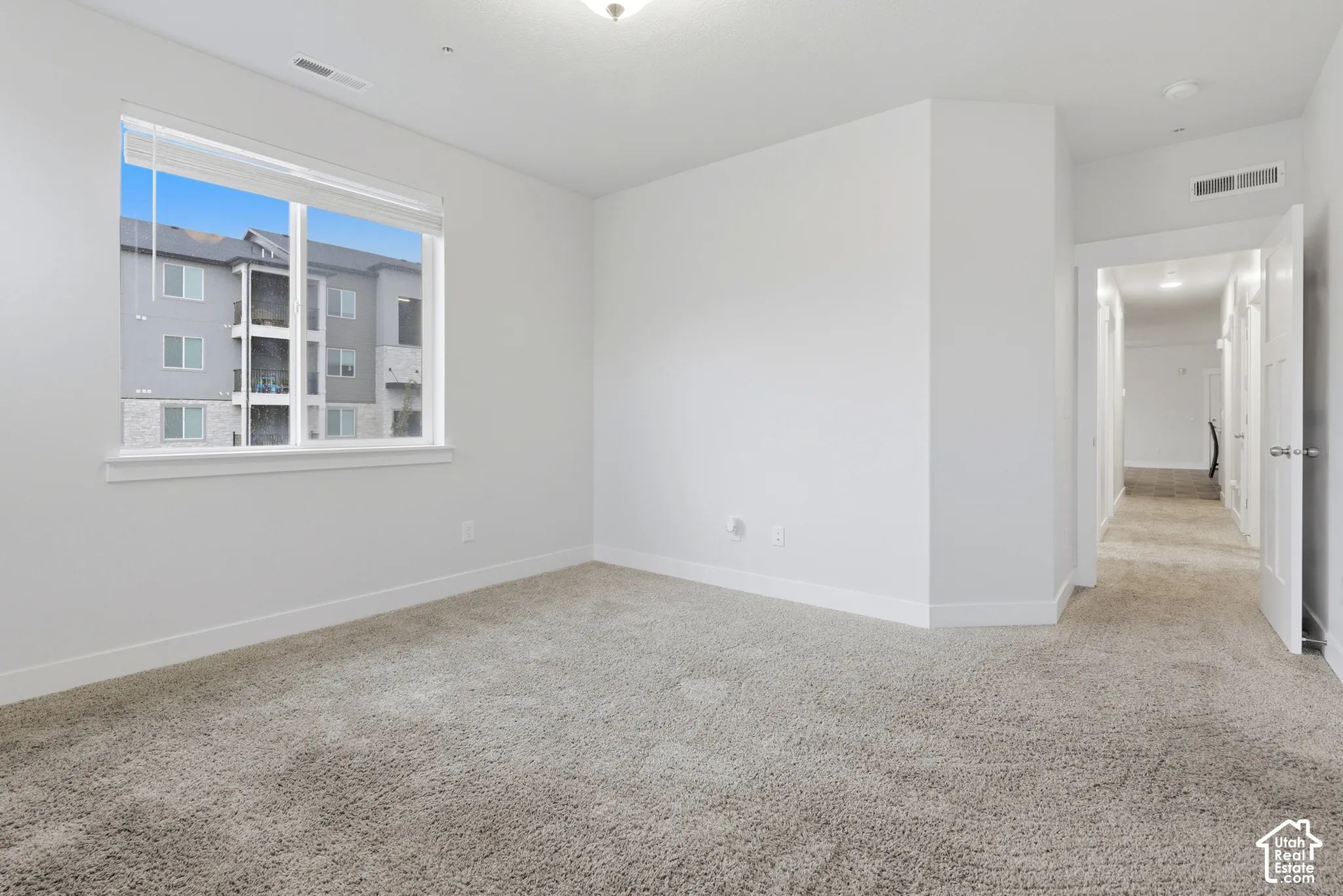 Neutral-toned carpeted flooring, white interior walls, and a large sliding window with blinds