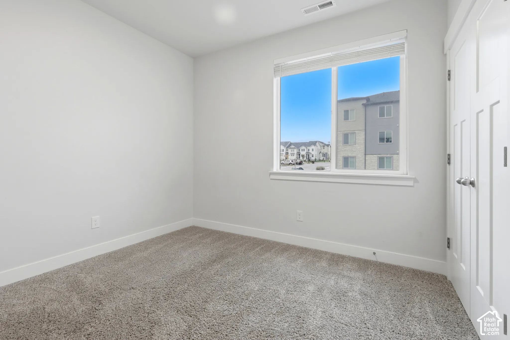 Room featuring neutral wall tones, plush wall-to-wall carpeting, a large sliding window with blinds, and double-door closet cabinetry