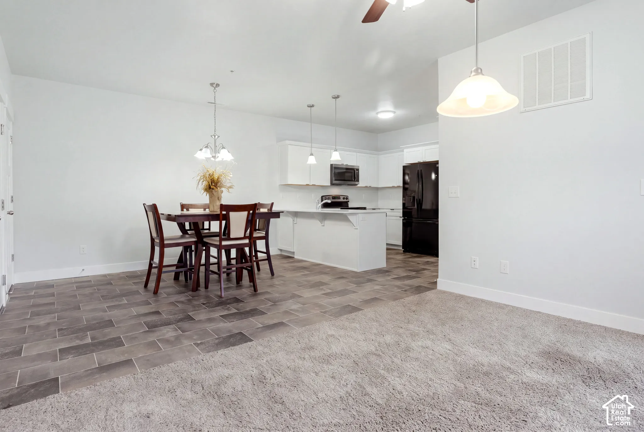 Kitchen featuring white cabinetry, an island with an extended counter, built-in microwave, and tile flooring, supplemented by carpeted flooring and multiple pendant light fixtures