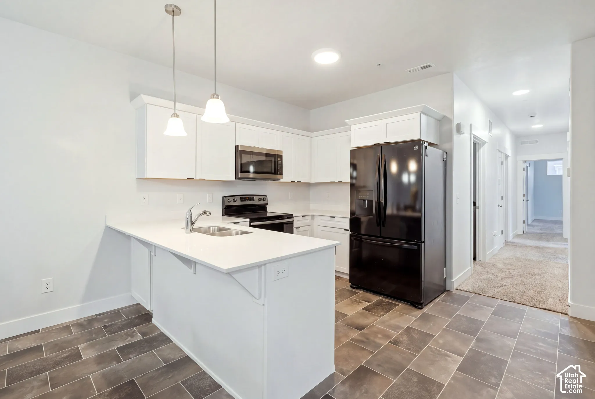 Kitchen featuring white cabinetry, solid-surface countertops, dual pendant lighting, and stainless steel appliances