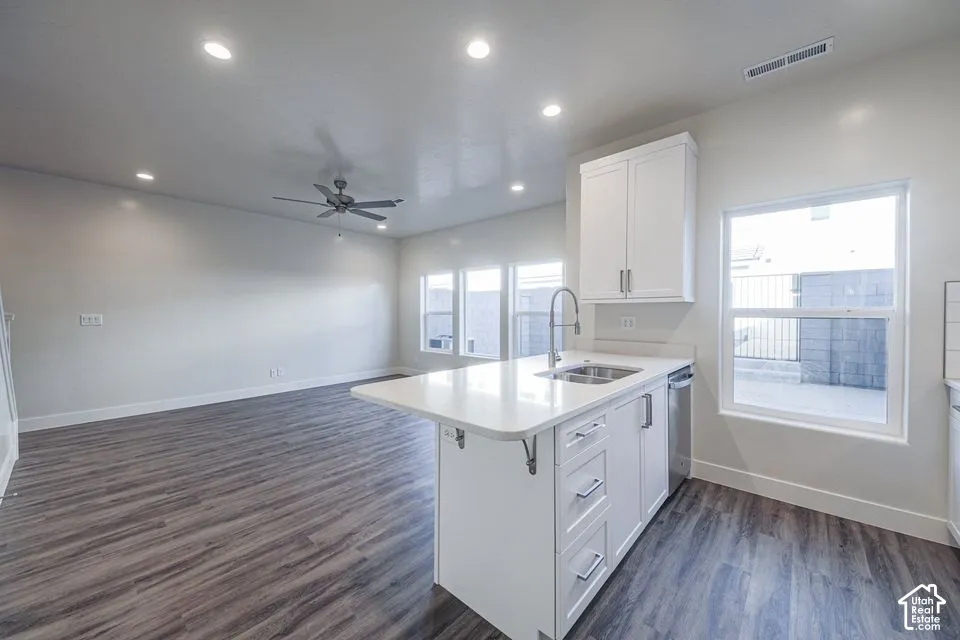 Kitchen island featuring a stone-composite countertop, undermount stainless steel sink, and white shaker-style cabinetry, complemented by recessed lighting and wood-finish flooring
