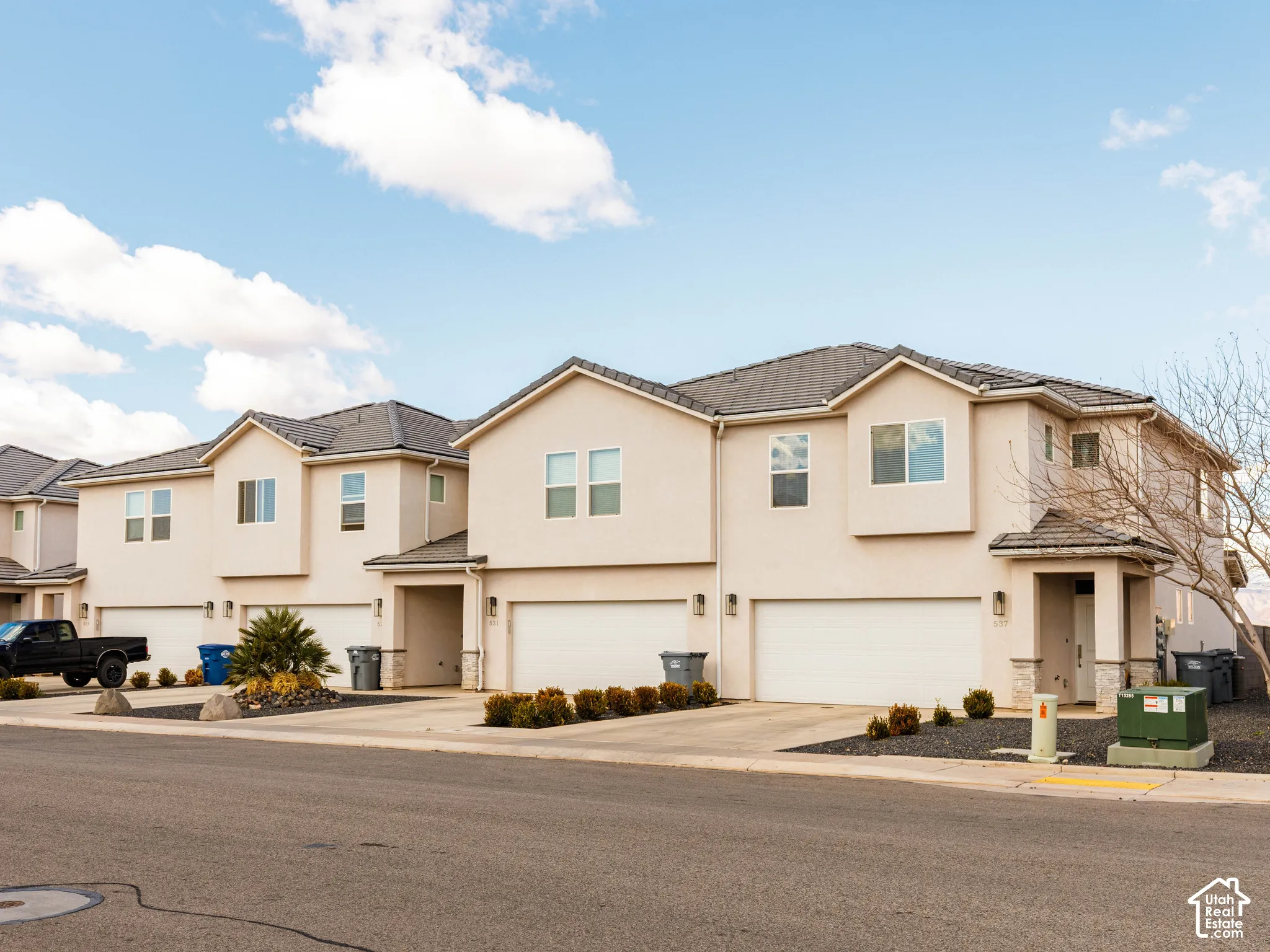 Two-story exterior featuring light-toned stucco siding, stone veneer accents, multi-gabled rooflines, and attached multi-car garages