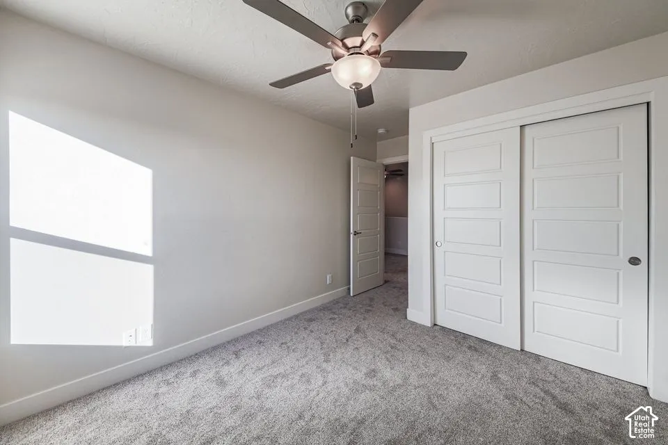 Neutral-toned interior featuring wall-to-wall carpeting, a ceiling fan with integrated lighting, and white five-panel sliding closet doors