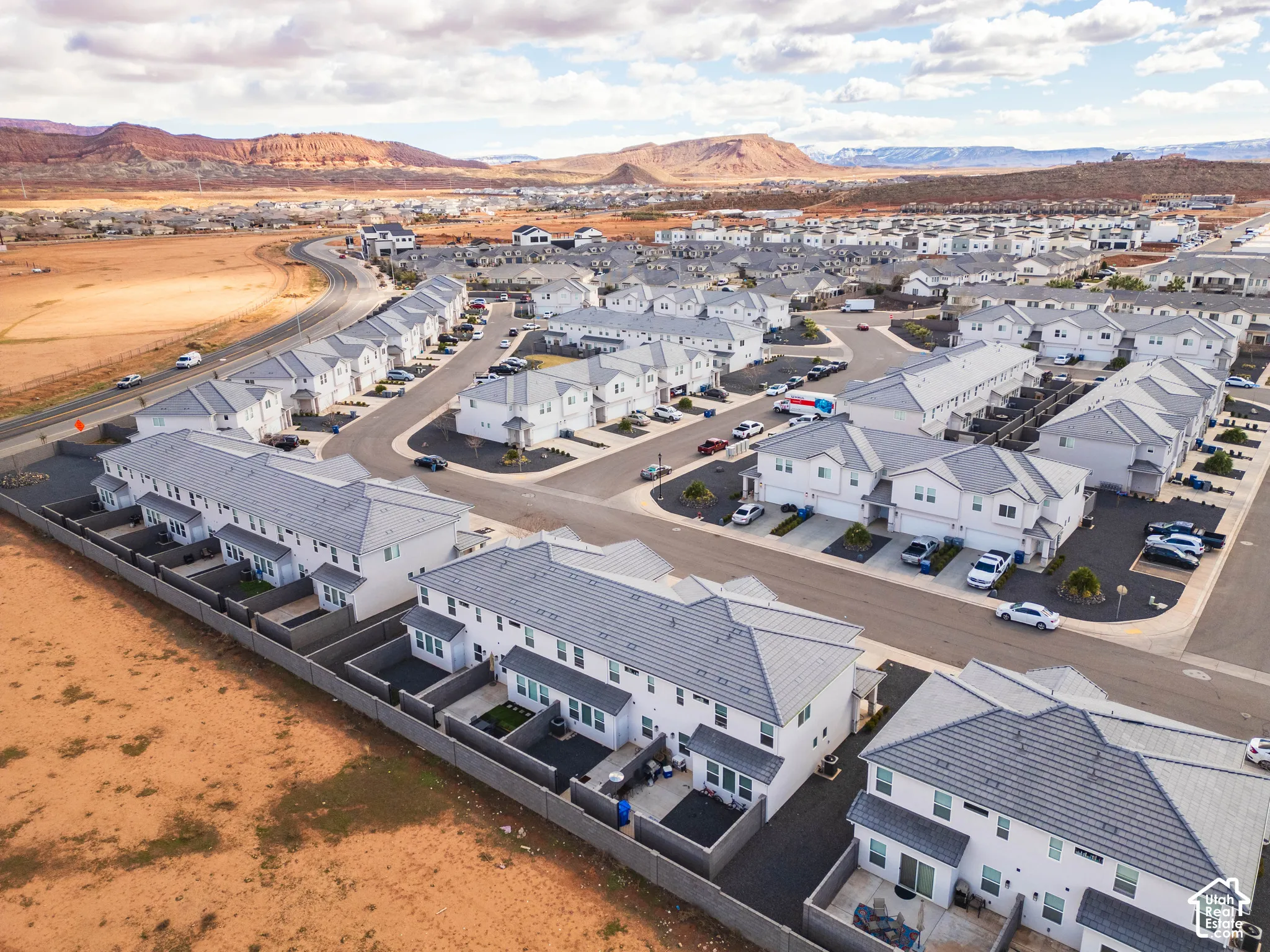Aerial perspective featuring multi-story residential structures with tile roofing, enclosed private patios, attached garages, and proximity to mountainous desert topography
