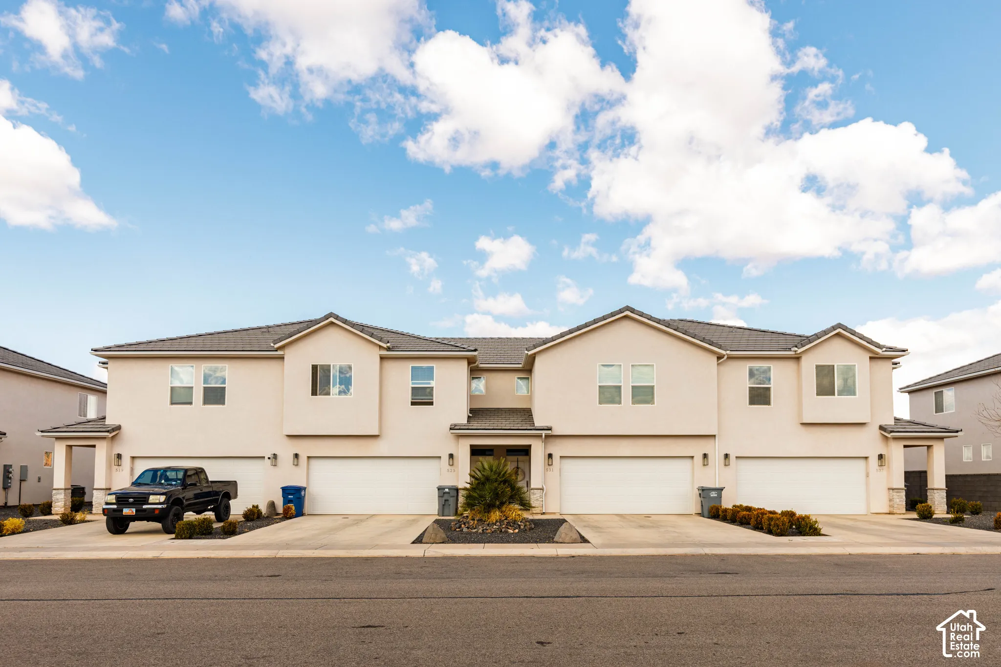 Multi-unit exterior featuring stucco siding, gabled rooflines, stone veneer accents, concrete driveways, and multi-car garage access