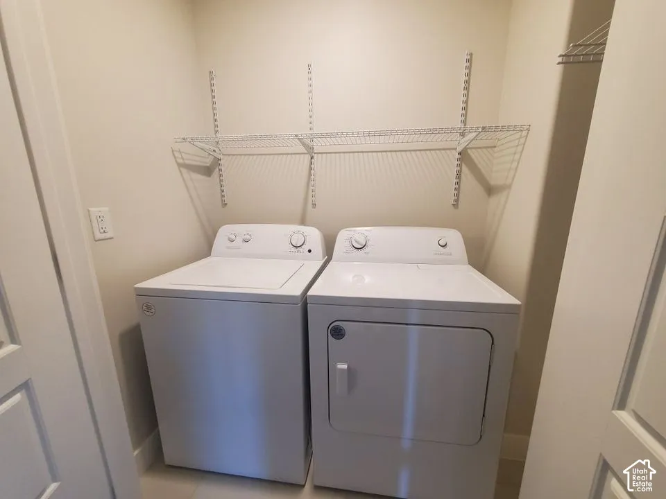 Laundry space featuring white top-loading washer and front-loading dryer, adjustable wall-mounted metal shelving, and neutral wall paint