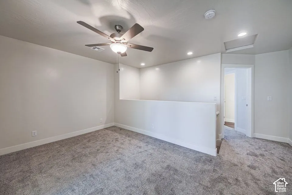 Neutral carpeting, recessed lighting, ceiling fan with integrated lighting, and a half-wall partition