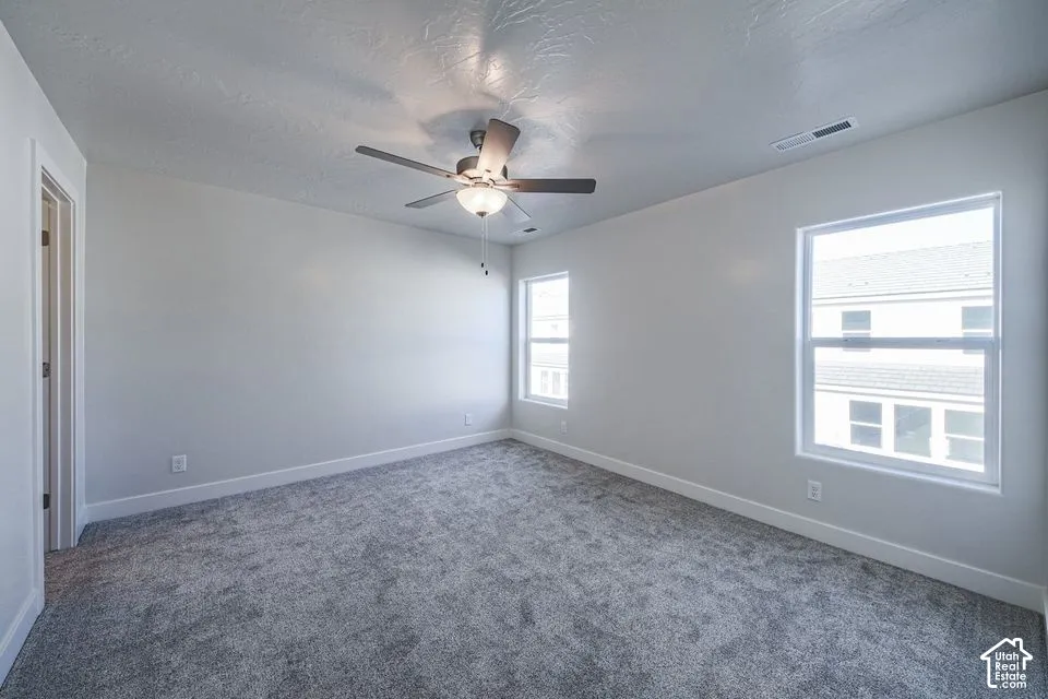 Room featuring neutral-toned carpeting, textured ceiling, central ceiling fan with integrated lighting, and dual windows