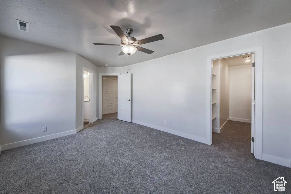Neutral-toned carpeted flooring, multi-speed ceiling fan with integrated lighting, and walk-in closet featuring built-in shelving