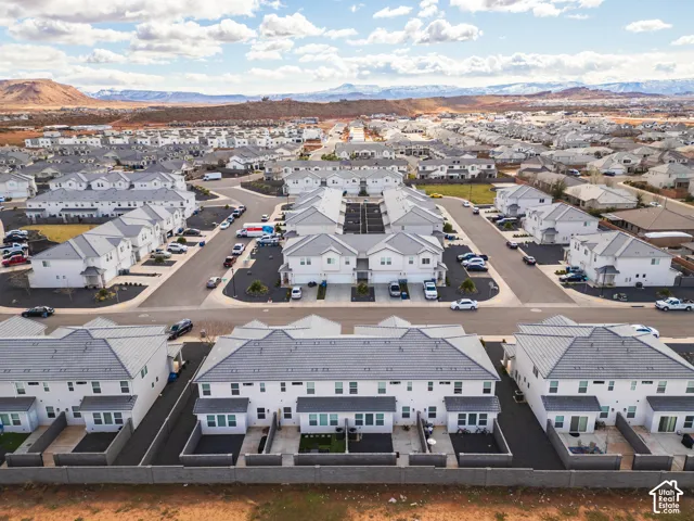 Multi-unit residential complex featuring uniform light-toned exteriors, shingled roofing, paved streets, and private rear patios enclosed by masonry walls with mountain backdrop