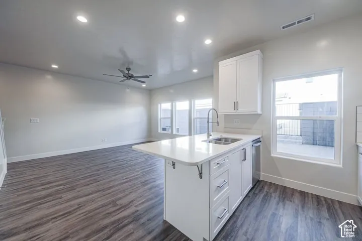 Kitchen island featuring a stone-composite countertop, undermount stainless steel sink, and white shaker-style cabinetry, complemented by recessed lighting and wood-finish flooring