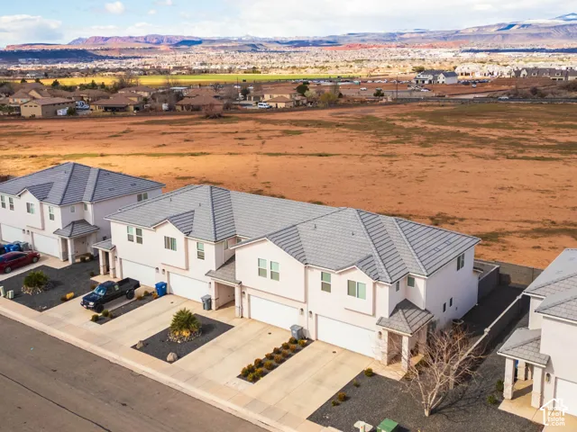 Multi-family residential structure featuring a tile roof, light-toned stucco exterior, attached multi-car garages, and concrete driveways with low-maintenance rock landscaping