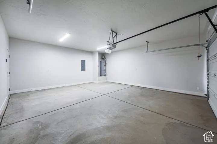 Finished garage featuring a concrete floor, integrated overhead lighting, an automated garage door opener, and a wall-mounted water heater