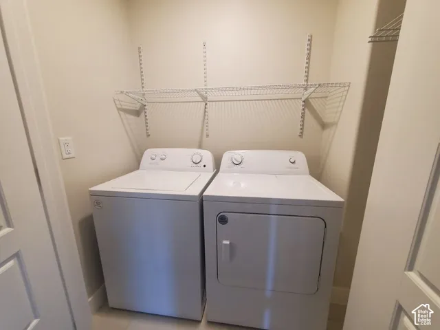 Laundry space featuring white top-loading washer and front-loading dryer, adjustable wall-mounted metal shelving, and neutral wall paint