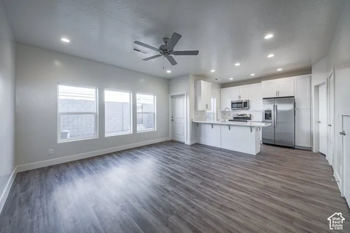 Open-concept interior featuring wood-finish flooring, recessed lighting, white cabinetry, a kitchen island, and stainless steel appliances