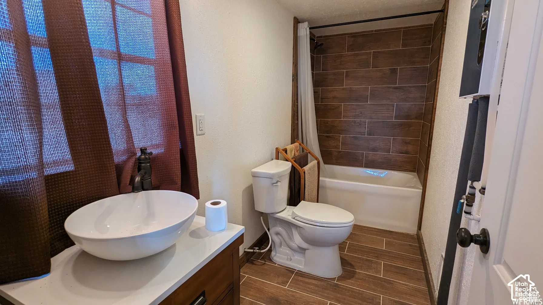 Bathroom featuring a vessel sink with a dark metal faucet, wood-finish tile flooring, and a tub surround clad in horizontal wood-finish tile