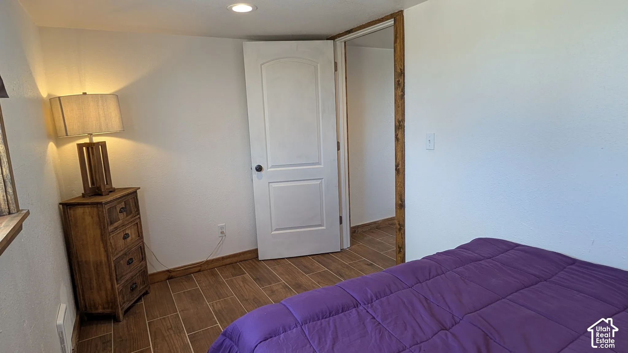 Wood-finish tile flooring, recessed ceiling lighting, and a white two-panel interior door with stained wood trim