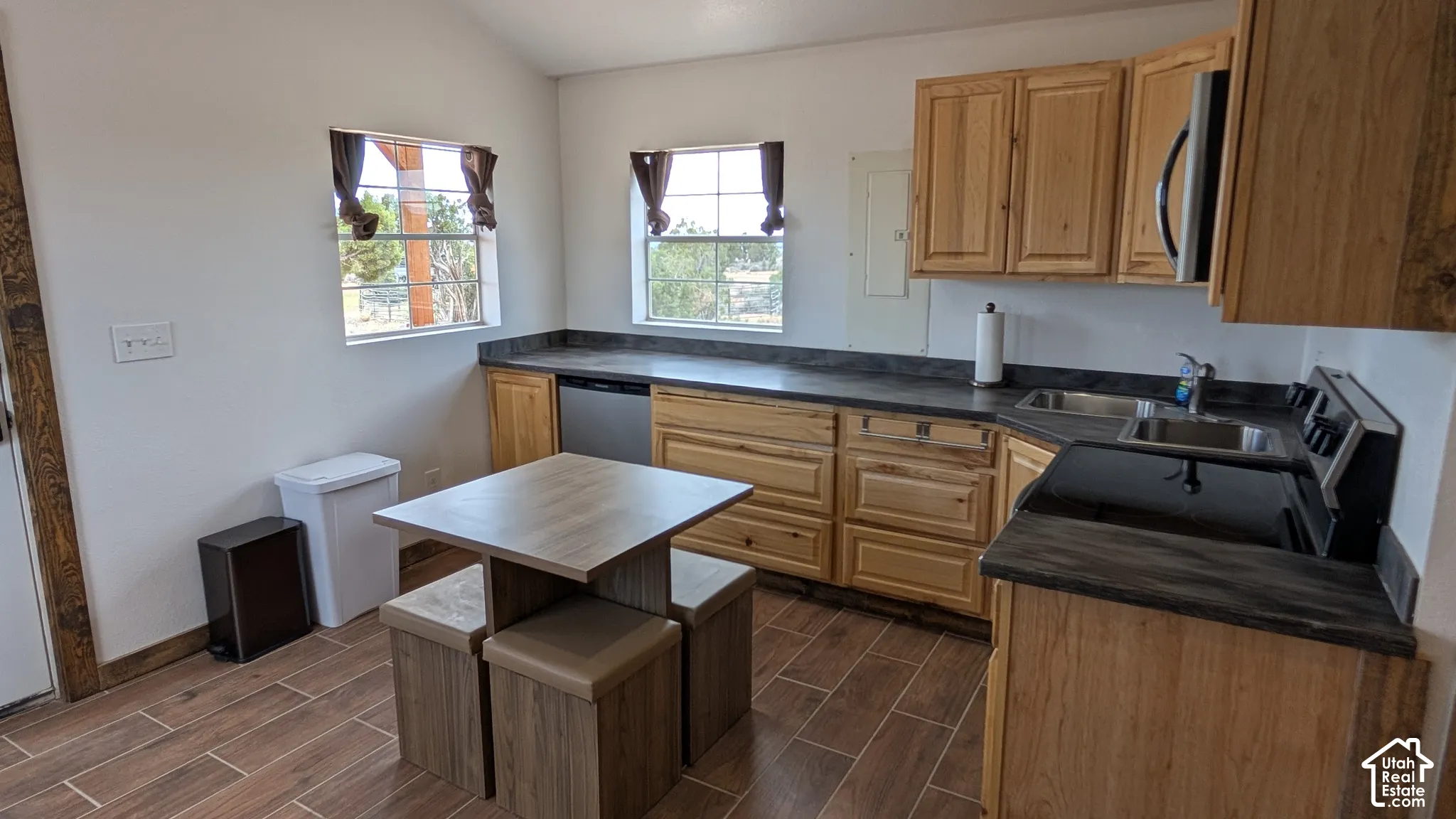 Kitchen featuring natural wood cabinetry, dark solid-surface countertops, wood-finish tile flooring, stainless steel appliances, and dual windows