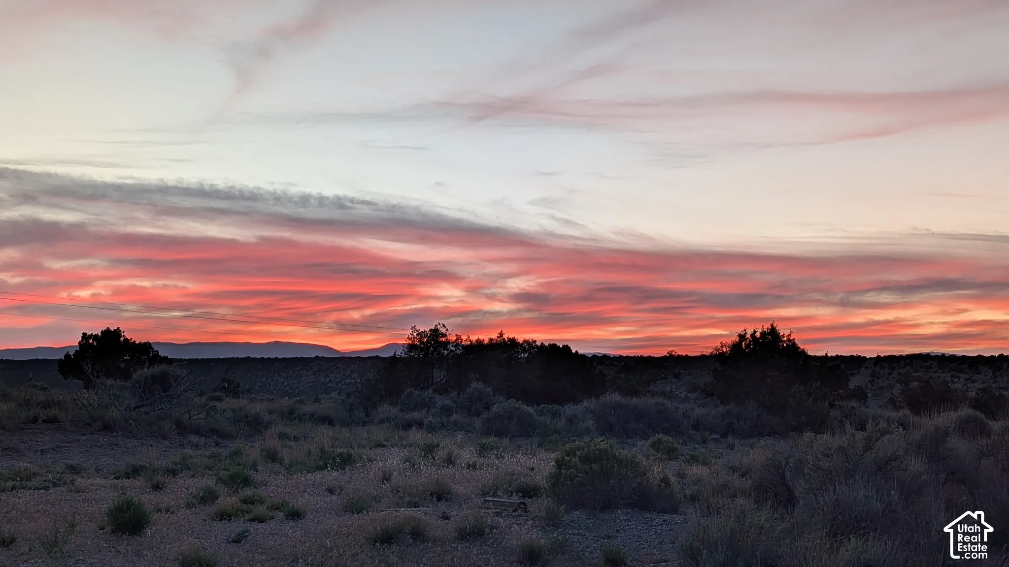 Expansive landscape featuring high-desert terrain, native scrub brush, and prominent mountain silhouettes under a colorful horizon